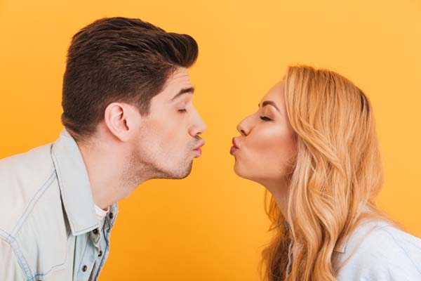 Ein Mann mit braunen Haaren und eine Frau mit blonden Haaren deuten einen Kuss an.