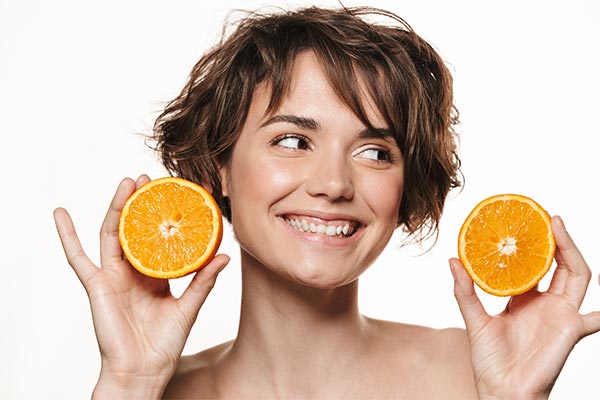 Eine braunhaarige Frau, die lächelnd 2 Orangenscheiben in den Händen hält