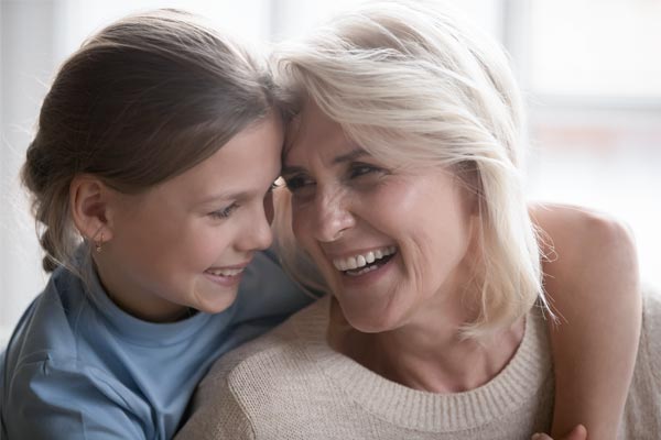 Ältere Frau mit hellen Haaren lacht mit einem jungen Kind mit dunkleren langen Haaren