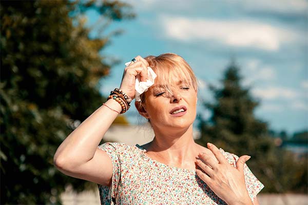 Frau kühlt gerötete Stirn bei Sonnenstich-Symptomen wie Kopfschmerzen und Schwindel in der Sonne. Frau kühlt gerötete Stirn bei Sonnenstich-Symptomen wie Kopfschmerzen und Schwindel in der Sonne.