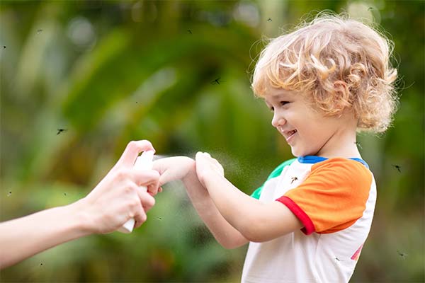 Ein kleiner Junge mit blonden Locken und bunten T-Shirt ist draußen in der Natur. Eine Person sprüht dem Jungen ein Spray auf seine Arme, da im Hintergurnd viele Insekten fliegen. Ein kleiner Junge mit blonden Locken und bunten T-Shirt ist draußen in der Natur. Eine Person sprüht dem Jungen ein Spray auf seine Arme, da im Hintergurnd viele Insekten fliegen.