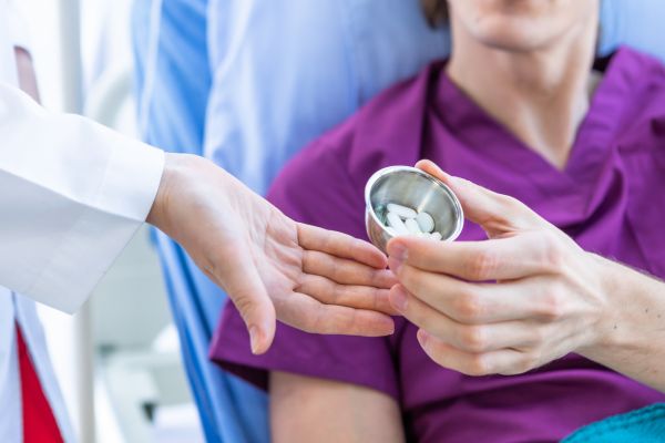 Eine Ärztin übergibt einem Krebspatienten seine Fentanyl-Dosis in Tablettenform. Er hat starke schmerzen und liegt im Krankenhausbett. Eine Ärztin übergibt einem Krebspatienten seine Fentanyl-Dosis in Tablettenform. Er hat starke schmerzen und liegt im Krankenhausbett.