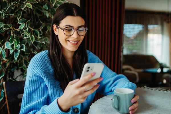 Lächelnde Frau hält ein Smartphone in der Hand. Eine braunhaarige Frau schaut auf ihr Smartphone.