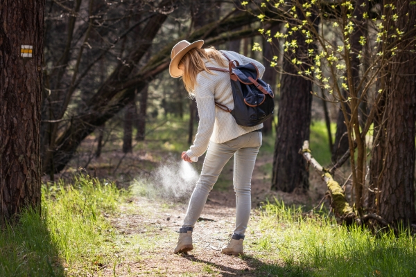 Eine Frau besprüht sich im Wald mit Insekten-Spray.