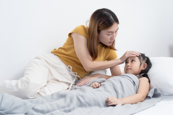 Mutter und Kind liegen im Bett, die Mutter prüft mit der Hand an der Sitrn des Kindes die Temperatur.