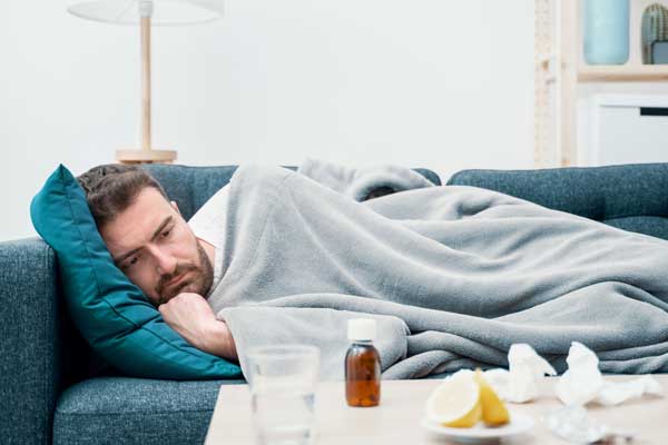 Ein braunhaariger Mann mit Influenza liegt erschöpft auf dem Sofa.