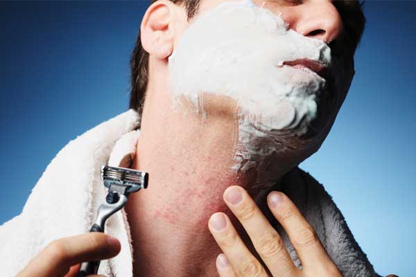 Ein weißer braunhaariger Mann rasiert sein Gesicht und hat Rasierschaum am Kinn.