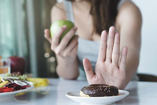 Eine Frau verzichtet wegen ihrer Diät auf einen Schoko-Donut und nimmt stattdessen einen grünen Apfel.