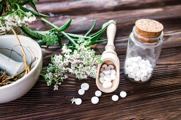 Weiße Baldriantabletten und eine Baldrianpflanze liegen auf einem dunklen Tisch. Weiße Baldriantabletten und eine Baldrianpflanze liegen auf einem dunklen Tisch.