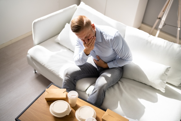 Ein Mann sitzt auf einem Sofa und hat Sodbrennen durch einen Calciummangel. Ein Mann sitzt auf einem Sofa und hat Sodbrennen durch einen Calciummangel.