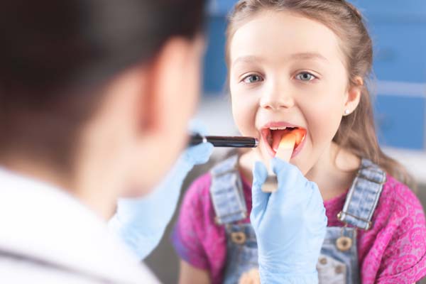 Ein Arzt untersucht ein Mädchen mit Verdacht auf eine Mandelentzündung, an ihrem Mund.