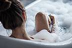 Eine braunhaarige Frau die sich in der Badewanne ihre Beine rasiert.