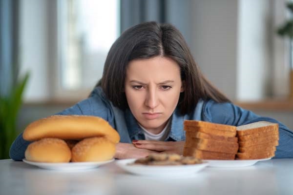 Eine Frau sitzt vor Produkten mit Gluten und kann sie wegen ihrer Zöliakie nicht essen.