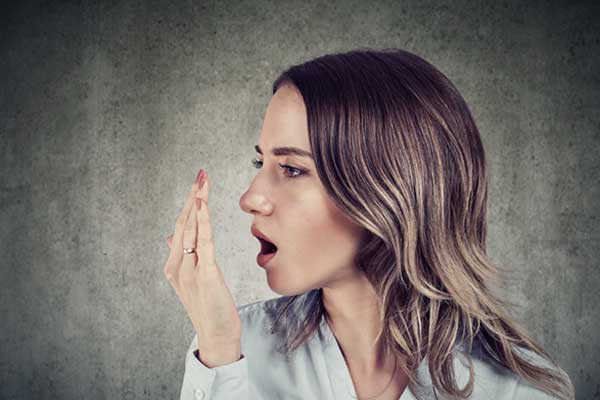 Eine Frau die mit ihrer Hand vor dem Mund testet, ob sie Mundgeruch hat