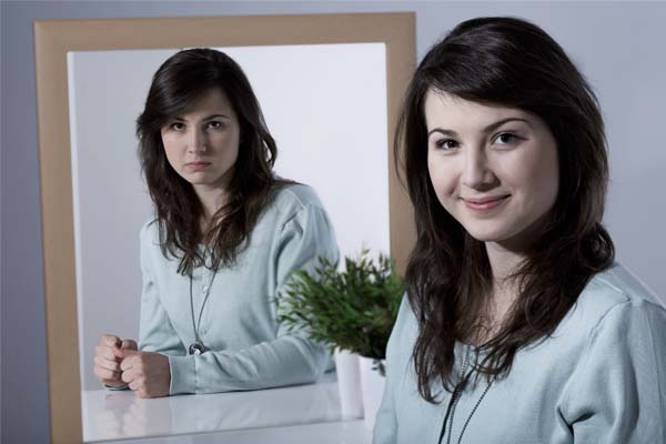 Eine Frau im Spiegel, die Gesichtsausdrücke vor und im Spiegel sind unterschiedlich.