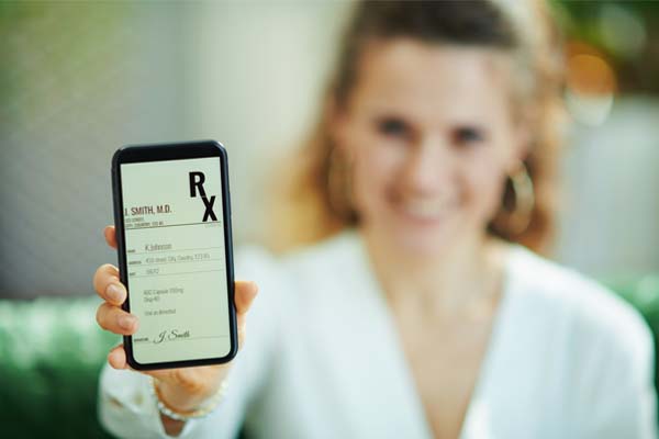 Eine braunhaarige Frau im Hintergrund, die ein E-Rezept auf dem Smartphone in den Vordergrund hält