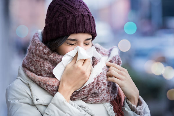 Eine winterlich angezogene Frau putzt sich ihre Nase.