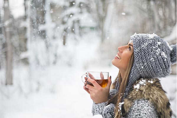 Frau steht im Schnee mit einer Tee-Tasse.