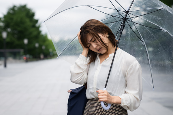 Frau mit Regenschirm hat hält sich ihren Kopf wegen Kopfschmerzen