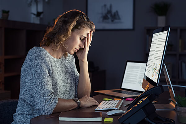 Frau sitzt abends im dunkeln vor dem Computer und hält vor Erschöpfung ihren Kopf.