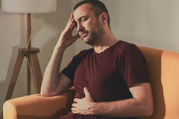 Ein Mann sitzt mit schmerzverzerrtem Gesicht auf dem Sofa und hält sich gleichzeitig den Kopf und den Bauch, was die enge Verbindung der Darm-Hirn-Achse bei Stress und Beschwerden verdeutlicht. Ein Mann sitzt mit schmerzverzerrtem Gesicht auf dem Sofa und hält sich gleichzeitig den Kopf und den Bauch, was die enge Verbindung der Darm-Hirn-Achse bei Stress und Beschwerden verdeutlicht.