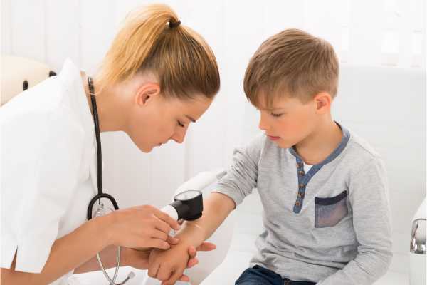 Eine Ärztin kontrolliert die Haut eines Kindes mit einer Lupe.