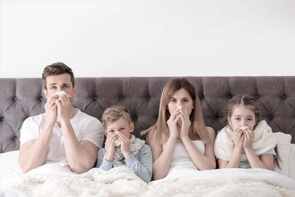 Eine vierköpfige Familie sitzt mit Erkältung im Bett