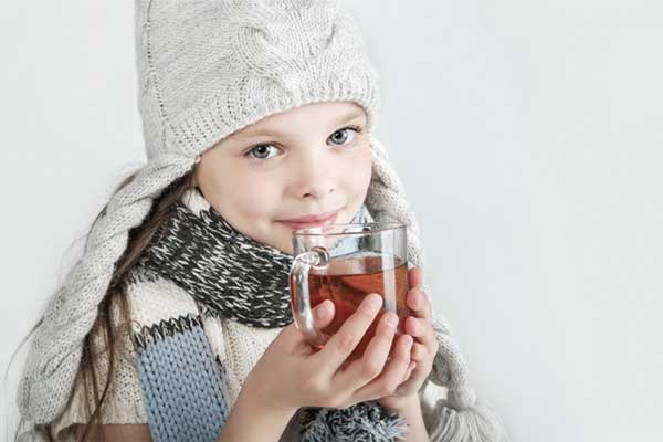 Ein Kind hält eine Tasse Tee in den Händen und trägt einen Schal um den Hals.
