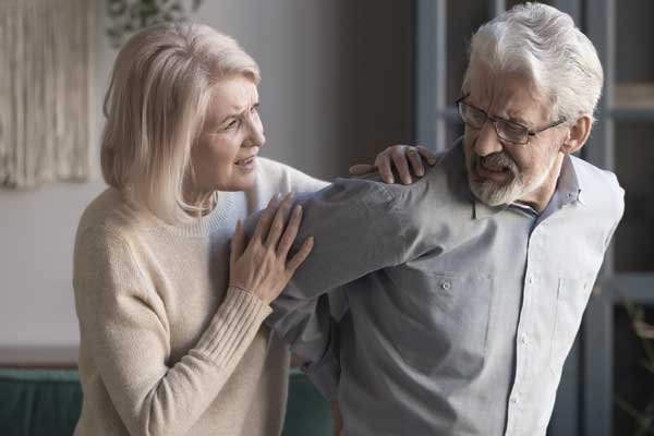 Frau hilft Mann mit Schmerzen im Rücken und stellt sich die Frage: Hexenschuss oder Bandscheibenvorfall?