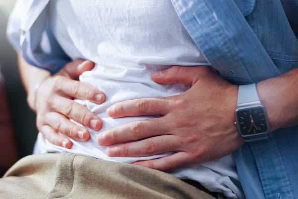 Eine Person hält sich mit beiden Händen den schmerzenden Oberbauch bei typischen Beschwerden einer Gastroparese (Magenlähmung). Eine Person hält sich mit beiden Händen den schmerzenden Oberbauch bei typischen Beschwerden einer Gastroparese (Magenlähmung).