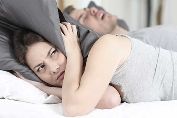 Mit einem Kissen auf dem Kopf versucht sich eine Frau vor dem lauten Schnarchen ihres Partners zu schützen. Mit einem Kissen auf dem Kopf versucht sich eine Frau vor dem lauten Schnarchen ihres Partners zu schützen.