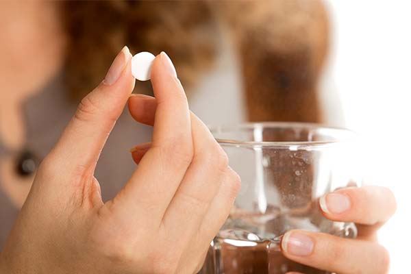 Eine Frau hält mit Ihrer rechten Hand eine weiße Tablette und mit der linken Hand ein Glas mit Wasser Eine Frau hält mit Ihrer rechten Hand eine weiße Tablette und mit der linken Hand ein Glas mit Wasser