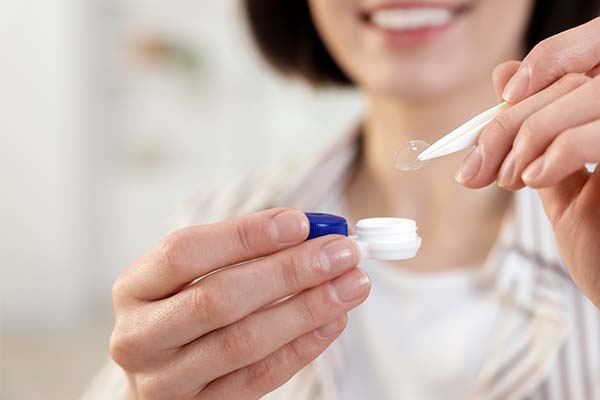 Eine Person hält eine Kontaktlinse mit einer Pinzette über einen geöffneten Aufbewahrungsbehälter. Eine Person hält eine Kontaktlinse mit einer Pinzette über einen geöffneten Aufbewahrungsbehälter.