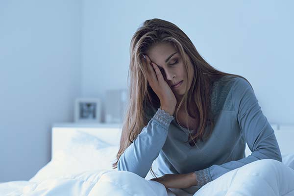 Eine erschöpfte Frau sitzt mit geschlossenen Augen im Bett und hält sich frustriert die Hand an die Stirn. Eine erschöpfte Frau sitzt mit geschlossenen Augen im Bett und hält sich frustriert die Hand an die Stirn.