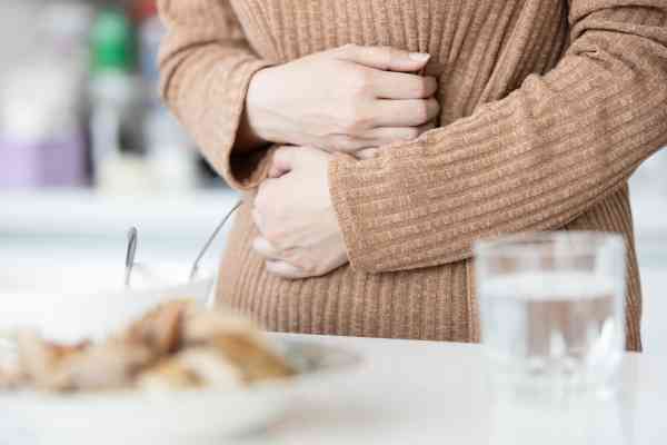 Person mit Magenbeschwerden nach dem Essen, die sich bei Völlegefühl oder Blähungen den schmerzenden Bauch hält. Person mit Magenbeschwerden nach dem Essen, die sich bei Völlegefühl oder Blähungen den schmerzenden Bauch hält.