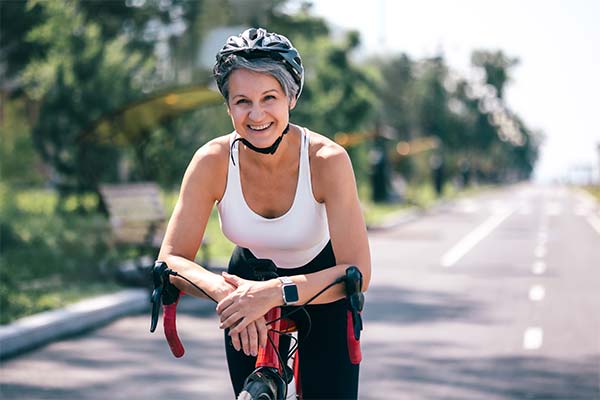 Eine glückliche, sportliche Frau in den Wechseljahren macht mit Helm und Rennrad eine Pause auf einem Fahrradweg und bleibt durch Bewegung fit. Eine glückliche, sportliche Frau in den Wechseljahren macht mit Helm und Rennrad eine Pause auf einem Fahrradweg und bleibt durch Bewegung fit.