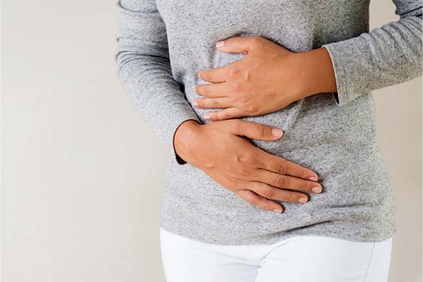 Eine Person hält sich mit beiden Händen den Bauch aufgrund von Beschwerden wie einem Blähbauch, Völlegefühl oder Bauchschmerzen. Eine Person hält sich mit beiden Händen den Bauch aufgrund von Beschwerden wie einem Blähbauch, Völlegefühl oder Bauchschmerzen.