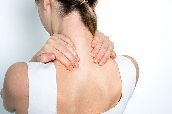 Eine Frau in einem weißen Top hält sich die Hände an ihren schmerzenden Nacken und die Schultern, was typische Fibromyalgie-Symptome verdeutlicht. Eine Frau in einem weißen Top hält sich die Hände an ihren schmerzenden Nacken und die Schultern, was typische Fibromyalgie-Symptome verdeutlicht.