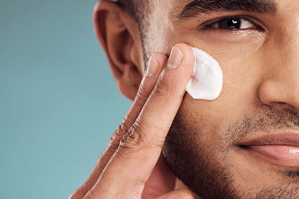Ein Mann streicht mit seinen Fingern eine Creme ins Gesicht. Ein Mann streicht mit seinen Fingern eine Creme ins Gesicht.
