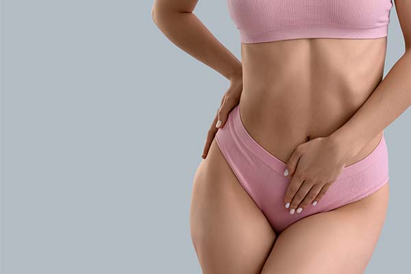 Eine Frau in rosa Unterwäsche hält ihre Hände an die Hüfte und den Bauch vor einem grauen Hintergrund. Eine Frau in rosa Unterwäsche hält ihre Hände an die Hüfte und den Bauch vor einem grauen Hintergrund.