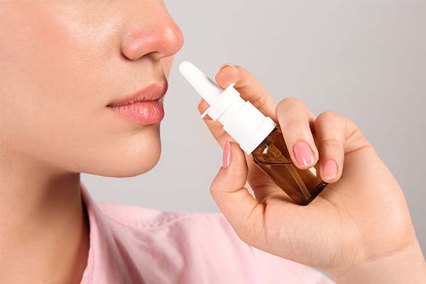 Eine Person hält ein braunes Nasenspray nah an die Nase, bereit zur Anwendung. Der Hintergrund ist neutral und hell. Eine Person hält ein braunes Nasenspray nah an die Nase, bereit zur Anwendung. Der Hintergrund ist neutral und hell.