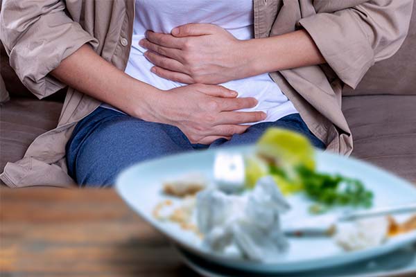 Person hält sich mit beiden Händen den schmerzenden Bauch, im Vordergrund steht ein Teller mit Essensresten. Person hält sich mit beiden Händen den schmerzenden Bauch, im Vordergrund steht ein Teller mit Essensresten.