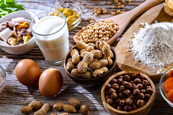 Verschiedene Lebensmittel wie Milch, Eier, Nüsse und Mehl, die häufig Allergien oder eine Nahrungsmittelunverträglichkeit auslösen können, arrangiert auf einem Holztisch. Verschiedene Lebensmittel wie Milch, Eier, Nüsse und Mehl, die häufig Allergien oder eine Nahrungsmittelunverträglichkeit auslösen können, arrangiert auf einem Holztisch.