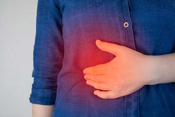 Eine Person hält sich die Hand schmerzgebeugt auf den Rippenbogen. Eine Person hält sich die Hand schmerzgebeugt auf den Rippenbogen.