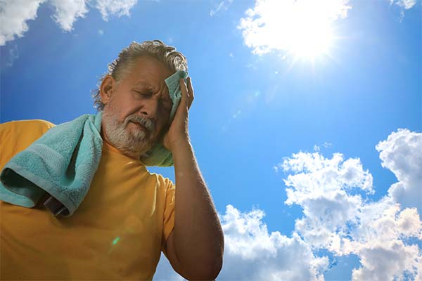 Ein älterer Mann im gelben T-Shirt ist in der Sonne und hält sich die Hand an die Stirn. Dabei kneift er die Augen fest zusammen. Ein älterer Mann im gelben T-Shirt ist in der Sonne und hält sich die Hand an die Stirn. Dabei kneift er die Augen fest zusammen.