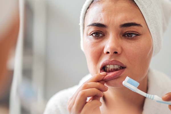 Eine Person betrachtet im Spiegel besorgt ihr Zahnfleisch, während sie eine Zahnbürste in der Hand hält. Eine Person betrachtet im Spiegel besorgt ihr Zahnfleisch, während sie eine Zahnbürste in der Hand hält.