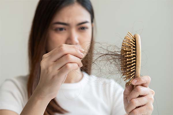 Eine junge Frau zieht ein Büschel Harre aus ihrer Haarbürste Eine junge Frau zieht ein Büschel Harre aus ihrer Haarbürste